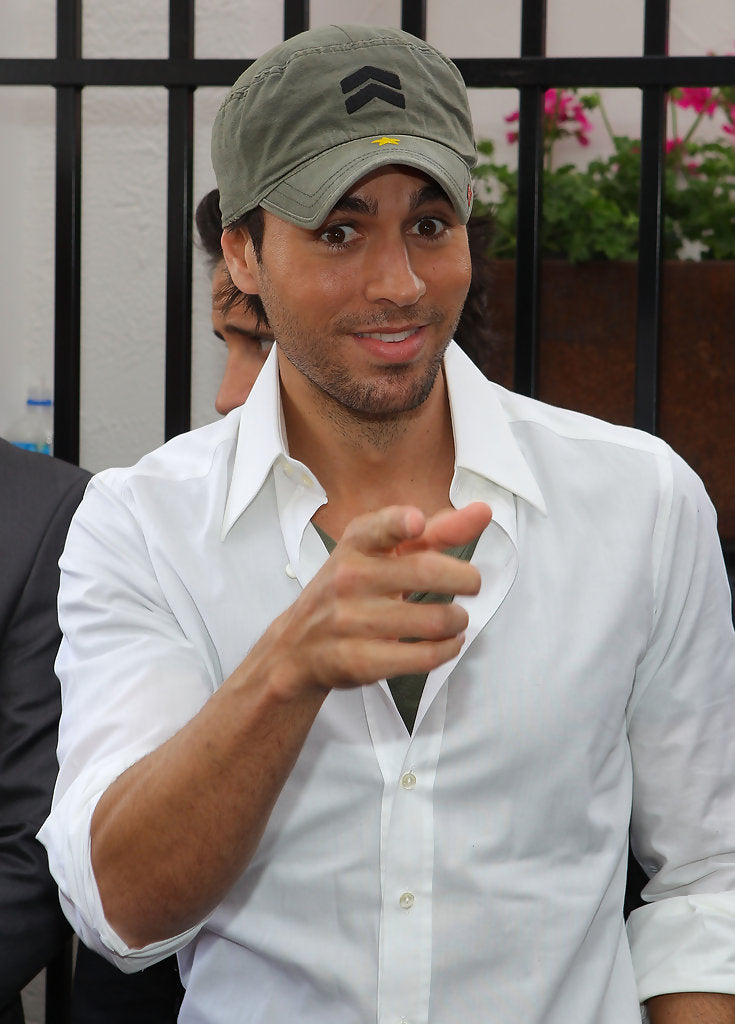 Enrique Iglesias na zewnątrz w oliwkowozielonej wojskowej czapce A. Kurtz Fritz z czarnym logo-szewronem i białej koszuli zapinanej na guziki.