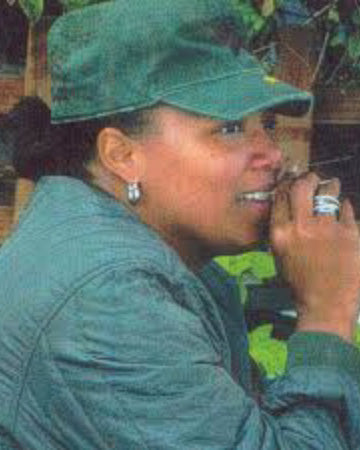 Queen Latifah w zielonej czapce kadetce Kurtz i zielonej kurtce, trzymająca mały przedmiot przy ustach.